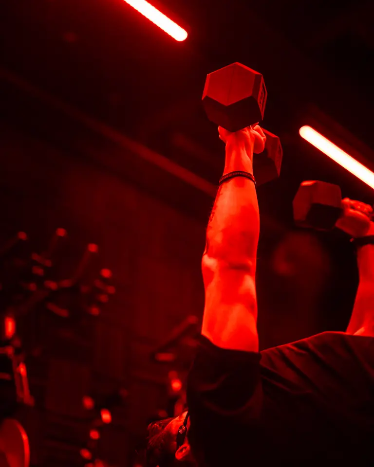 Coach levantando una mancuerna bajo un tubo de luz roja